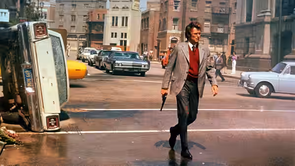Harry (Clint Eastwood) walks through an intersection holding a revolver