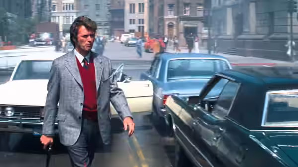 Harry (Clint Eastwood) walks between parked cars on a city street