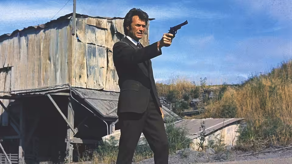 Harry (Clint Eastwood) aims a revolver beside a wooden industrial building