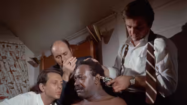 Sweetback (Melvin Van Peebles) is restrained as a man presses a gun to his head