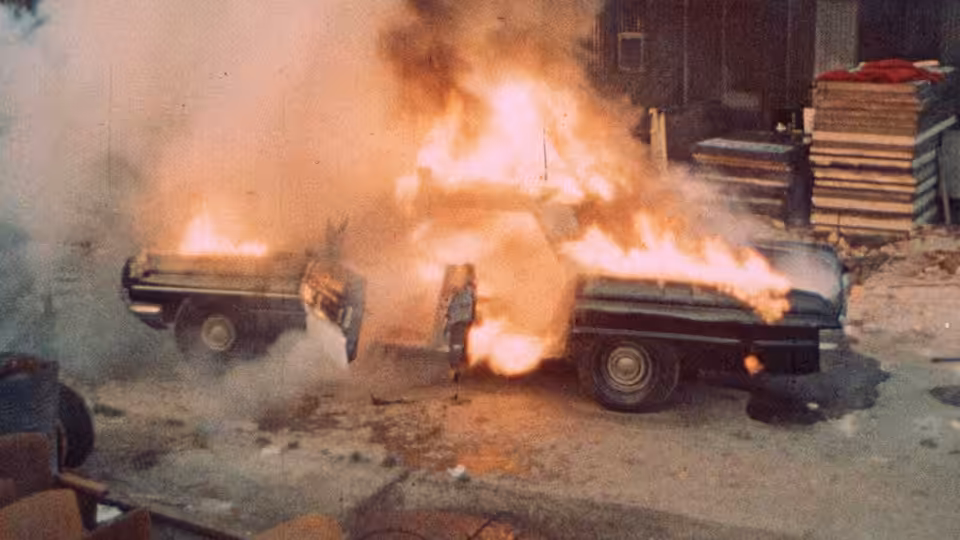 A car burns in the street as flames pour from its windows