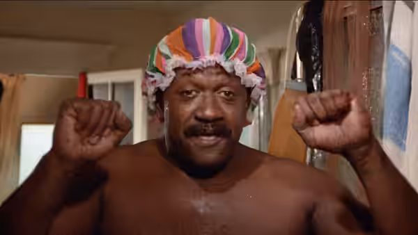 A shirtless man wearing a colorful shower cap raises both fists