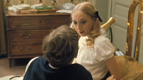 A young woman in a white blouse faces a seated boy in a bedroom