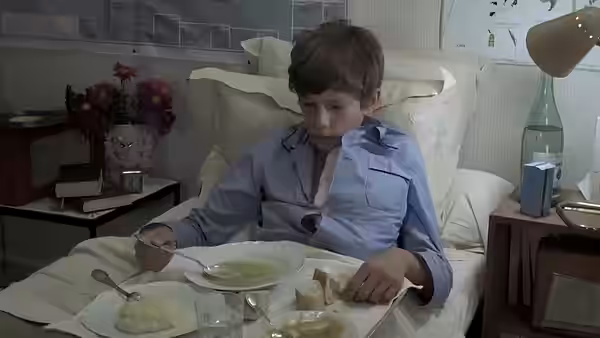 A boy in pajamas eats a meal in bed