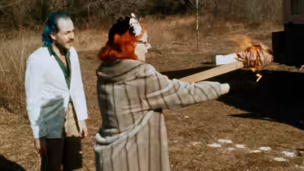 Connie Marble (Mink Stole) points toward a burning object as a man watches