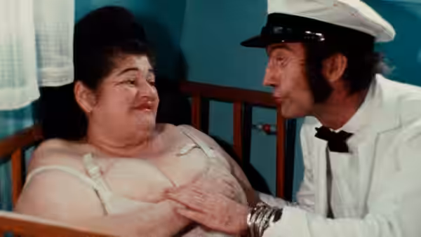 Edie (Edith Massey) reclines in bed as a uniformed man leans toward her