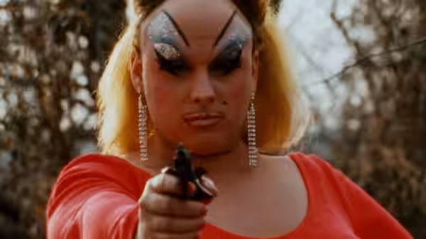 Divine (Divine) points a handgun directly ahead while wearing a red dress