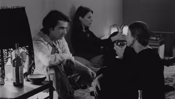 A seated man talks with two companions in a furnished room