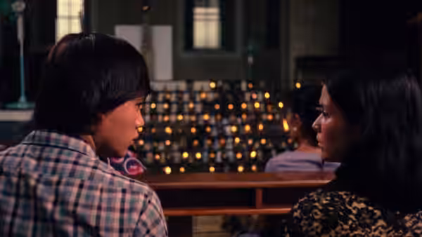 A man and woman talk across a table in a dimly lit bar