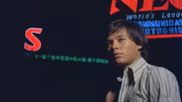 A young man stands beneath illuminated signs on a city street