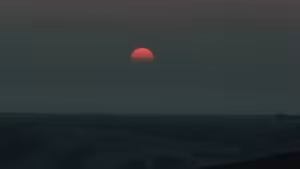 A red sun sinks toward the horizon above a dark, flat landscape