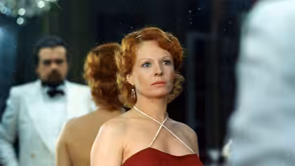 Anne-Marie Stretter (Delphine Seyrig) in a red dress faces a mirror as a servant stands behind her