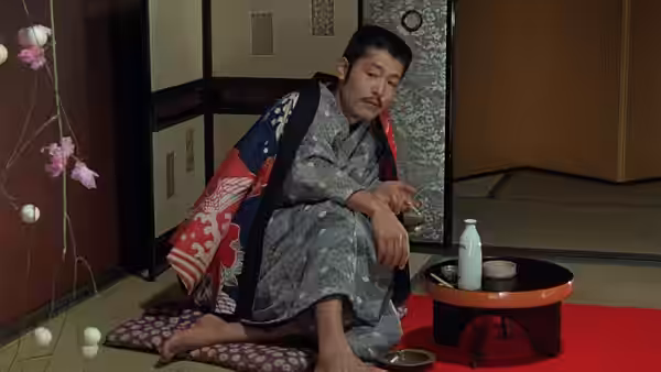 Kichizo Ishida (Tatsuya Fuji) sits alone on a cushion beside a low table