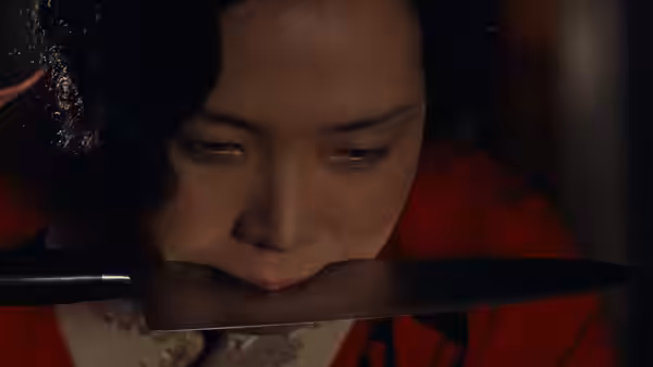 Sada Abe holds a knife between her lips in a dim room