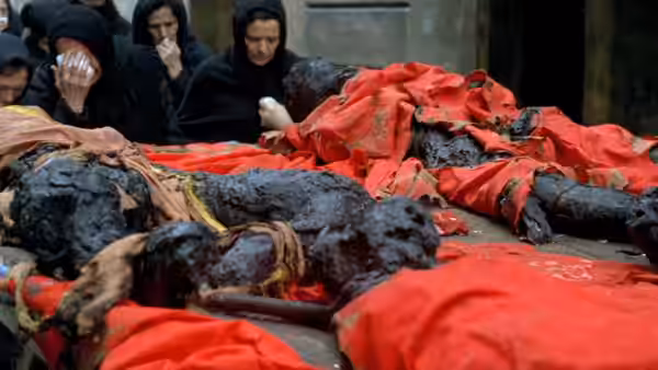 Mourners gather around bodies draped in red cloth in a courtyard