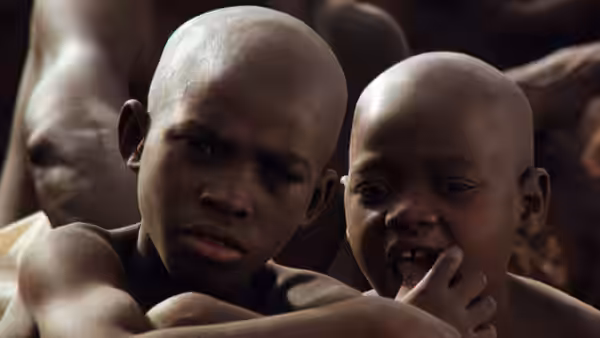 Two boys sit among a group of people, one touching his mouth