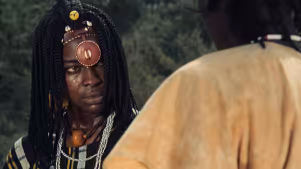 A young man in beaded braids faces another man outdoors
