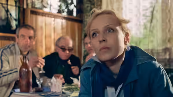 Agnieszka (Krystyna Janda) leans forward at a table as men sit behind her