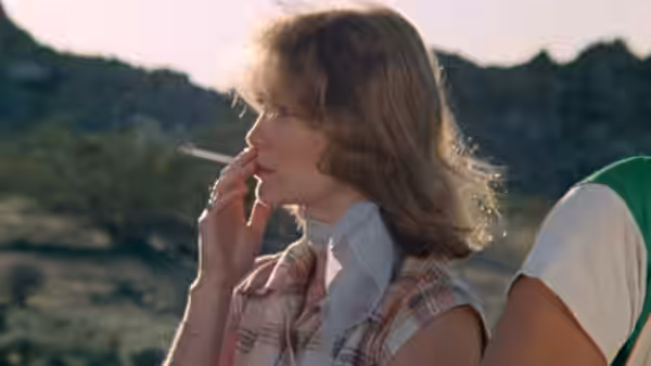 Brenda Carter (Susan Lanier) smokes outdoors beside a man in the hills