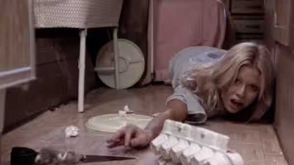 Brenda Carter (Susan Lanier) crawls across a kitchen floor toward a knife