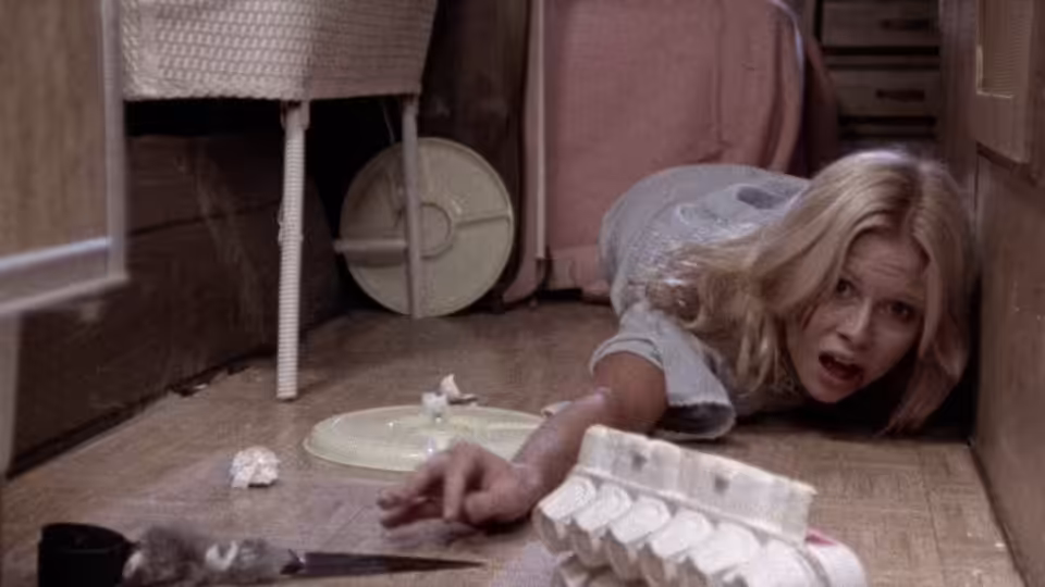 Brenda Carter (Susan Lanier) crawls across a kitchen floor toward a knife