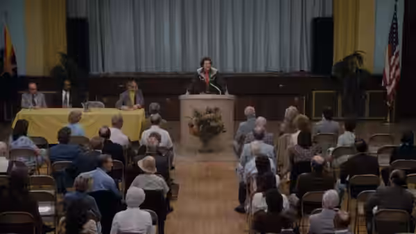 Albert Brooks (Albert Brooks) addresses an audience from a podium in a meeting hall