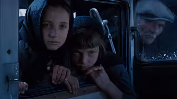 Two children peer from a vehicle window as an elderly man looks in