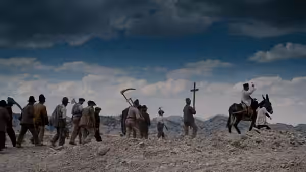 Villagers walk across a rocky hillside behind a man riding a donkey