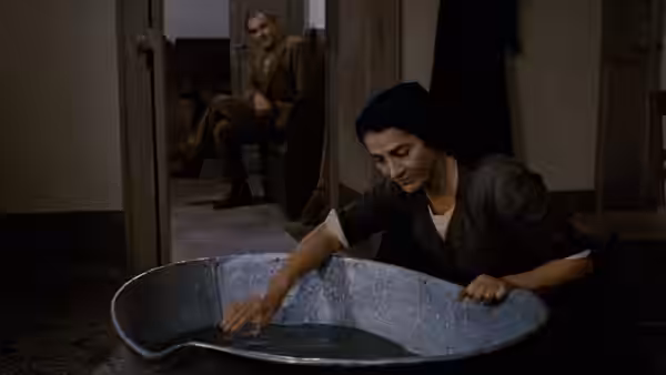 A woman washes clothes in a metal tub while Carlo Levi watches from a doorway