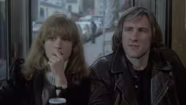 Nelly (Isabelle Huppert) touches her lips as Loulou (Gérard Depardieu) sits beside her in a café