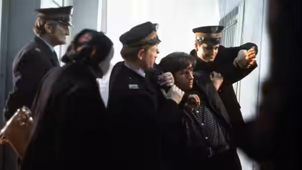 Uniformed officers escort a woman through a building corridor
