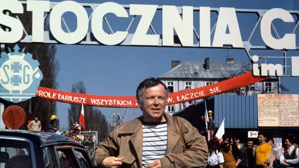 Winkel (Marian Opania) stands outside the Gdańsk Shipyard entrance amid workers and banners