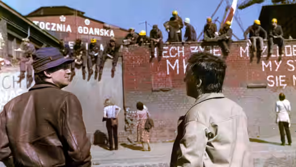 Two men face shipyard workers gathered behind a wall covered in protest slogans