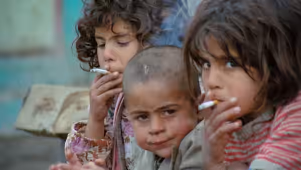 Three children crowd together, two smoking cigarettes and looking toward the camera