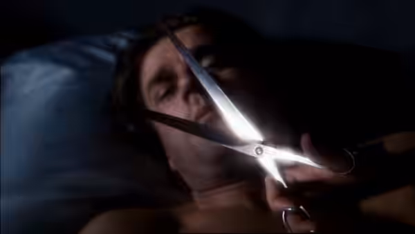 A man lies on a pillow as open scissors hover across his face