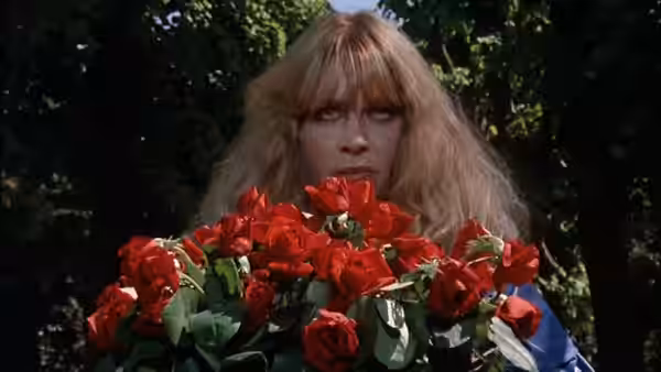 A blonde woman holds a large bouquet of red roses outdoors