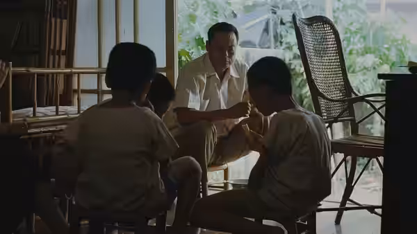 A seated man talks with several boys gathered around him in a home