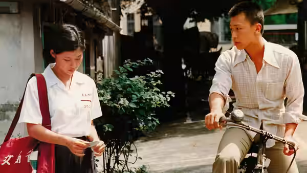 A schoolgirl studies a paper while a young man watches from his bicycle