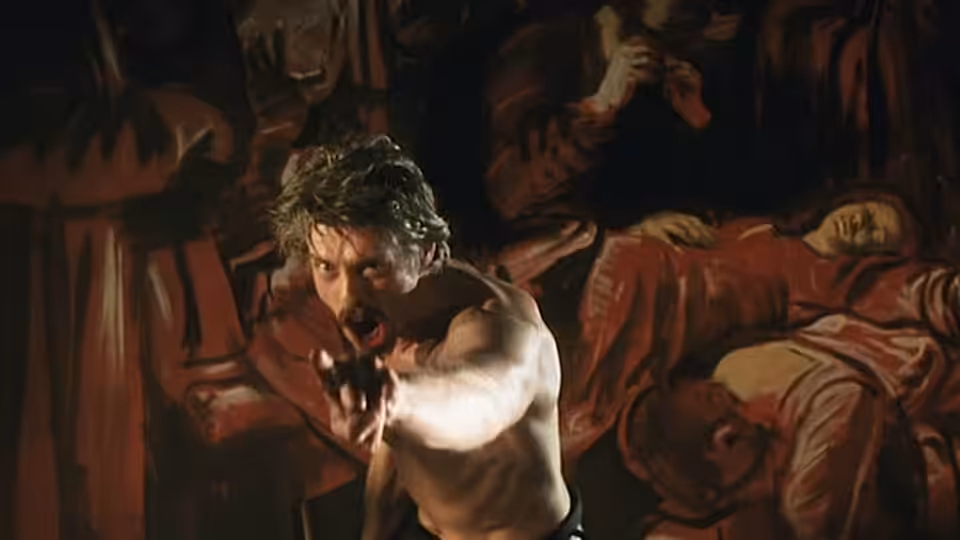 Caravaggio (Nigel Terry) thrusts a dagger forward before a bed of reclining figures