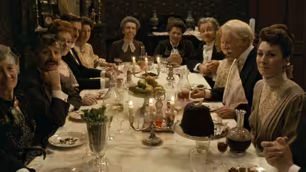 Guests gather around a candlelit dinner table in a Victorian drawing room
