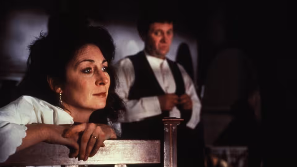 Gretta Conroy (Anjelica Huston) leans over a chair as a man stands behind her