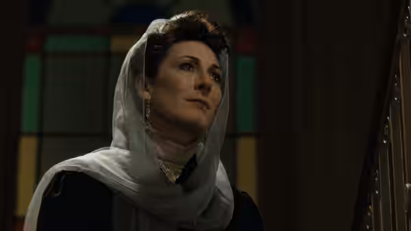 Gretta Conroy (Anjelica Huston) stands beneath a stained-glass window wearing a white scarf