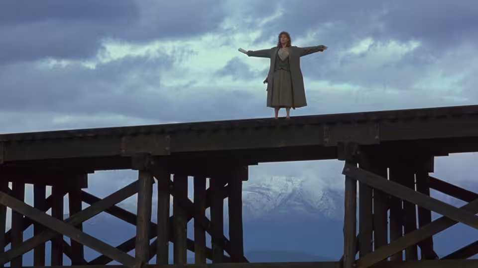 Sylvie Fisher (Christine Lahti) stands with her arms outstretched atop a wooden trestle bridge