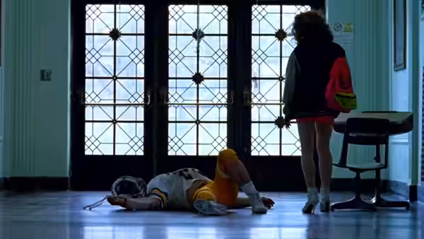 A young woman stands by the doors while another person lies on the floor