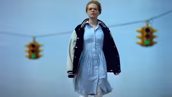 Maria Coughlin (Adrienne Shelly) stands beneath traffic lights in a varsity jacket and pale dress