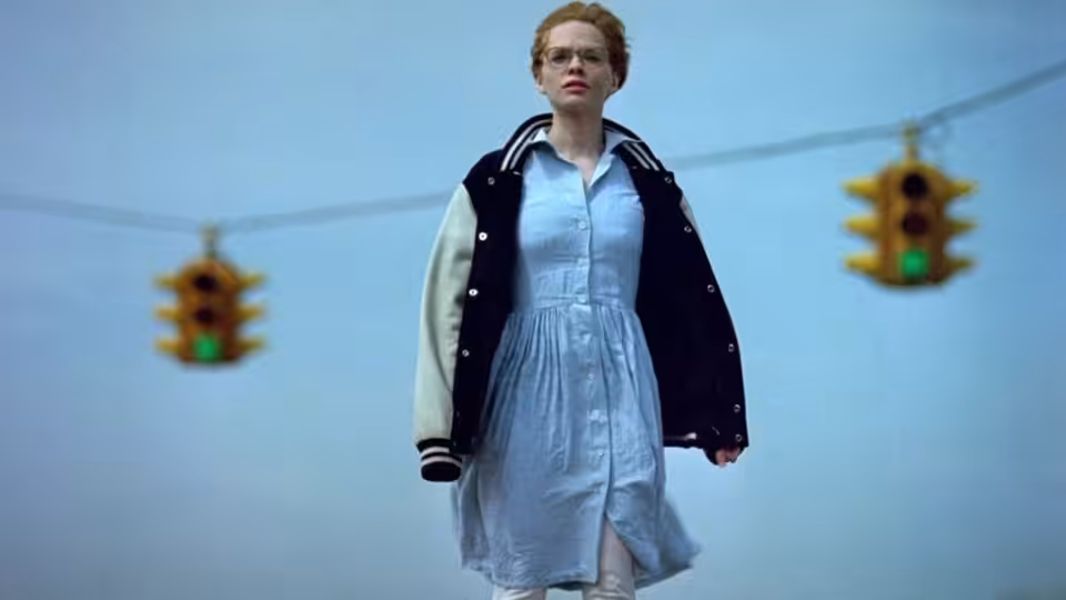 Maria Coughlin (Adrienne Shelly) stands beneath traffic lights in a varsity jacket and pale dress