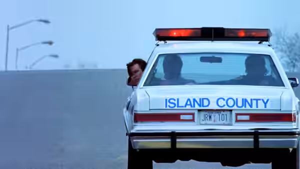 A man peers around the back of an Island County police car
