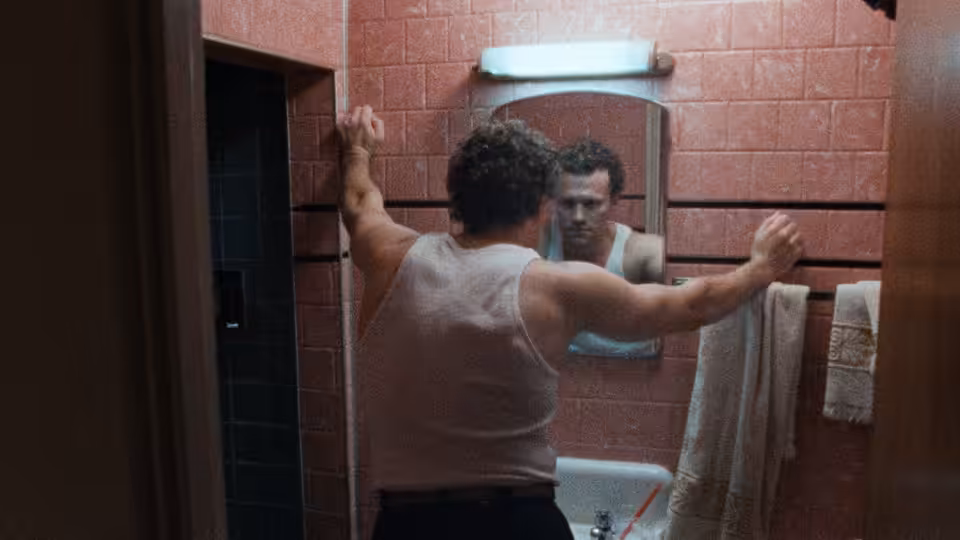 Henry (Michael Rooker) braces himself against a bathroom wall, studying his reflection in the mirror