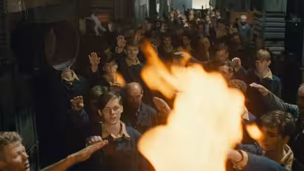 Boys raise their hands around a fire in a crowded room