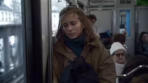 Félicie rides a tram, clutching a bag among the passengers